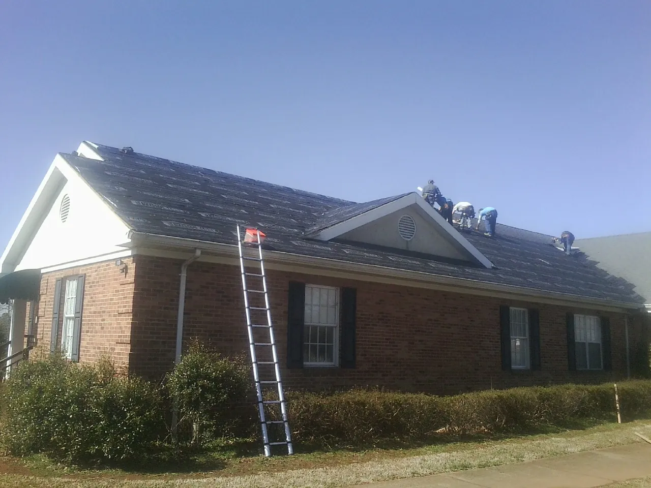 Crew tearing shingles off a brick ranch roof with a ladder set — Metal Roof Repair work by our crew in Florence